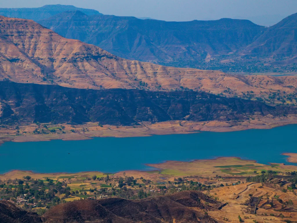 Sydney Point Panchgani during sunny weather, featuring Kate's Point lake, Sahyadri mountains, fields, perfect scenic adventure, Maharashtra tour packages.