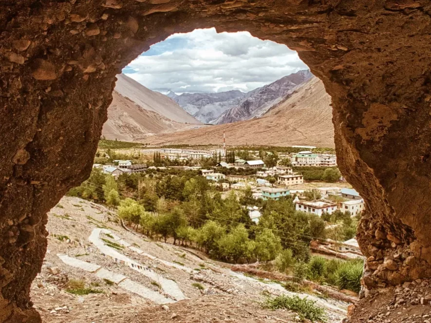 Tabo Caves panoramic view at Tabo Spiti Valley during partly cloudy skies, featuring villages greenery barren mountains through cave frame, perfect adventure experience Spiti Valley Himachal tour package.
