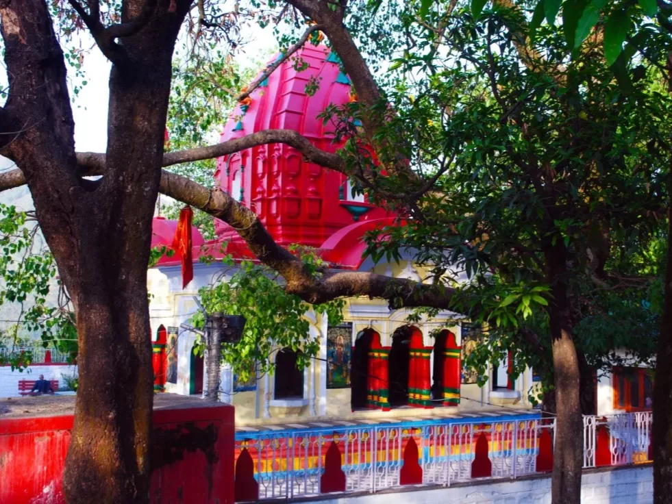 Tarna Devi Temple Mandi vibrant red curved Bengali roof temple tree framed red doors rainbow fence green trees cloudy sky, perfect Kali Mata hill temple darshan, Himachal Pradesh tour packages.