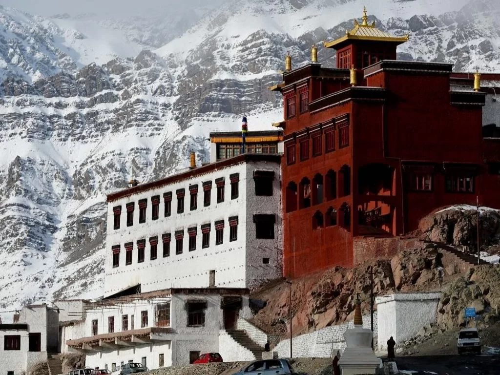 Red and white Tashi Thanyang Monastery at Nako during winter sunny day, featuring golden roofs, snowy peaks, rocky base, perfect spiritual Himachal Pradesh tour package.