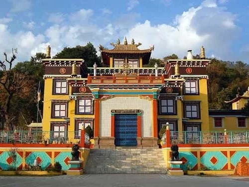 Front view of Tayul Monastery in Keylong showcasing a vibrant Tibetan-style structure with golden rooftop details, colorful facade, central blue entrance gate, and decorative boundary walls against a hillside backdrop.