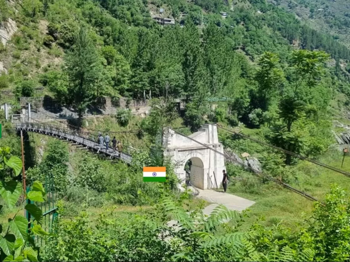 Teetwal Village LoC suspension bridge gate during sunny day Kashmir, featuring iron truss people Indian flag white arch lush pine hills backdrop, perfect Kashmir tour packages.