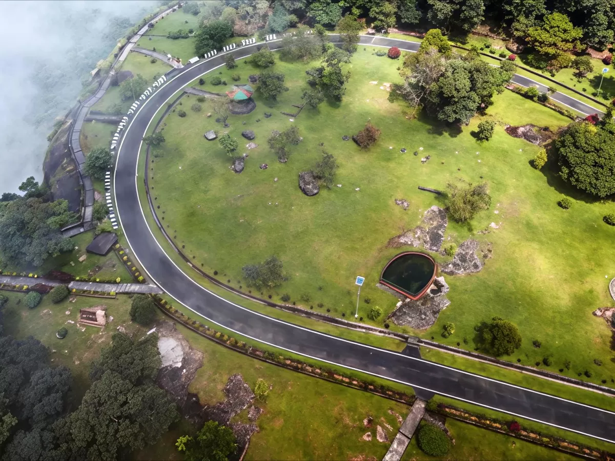 Thangkharang Park Cherrapunji during misty morning, featuring aerial view green lawns winding roads pavilion sacred pool trees lake backdrop, perfect nature park experience Cherrapunji Meghalaya tour package.