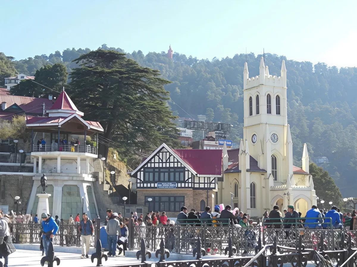 Crowded tourists at Christ Church The Ridge Shimla during sunny day, featuring Gothic tower half-timbered buildings statue fountain deodar hills Jakhoo Temple, perfect heritage cultural experience Himachal Pradesh tour packages.