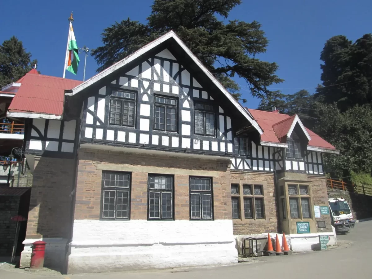 Tourist Information Centre at The Ridge Shimla during sunny day, featuring half-timbered colonial architecture Indian flag deodar pines brick base signage van cones hills, perfect heritage cultural experience Himachal Pradesh tour packages.