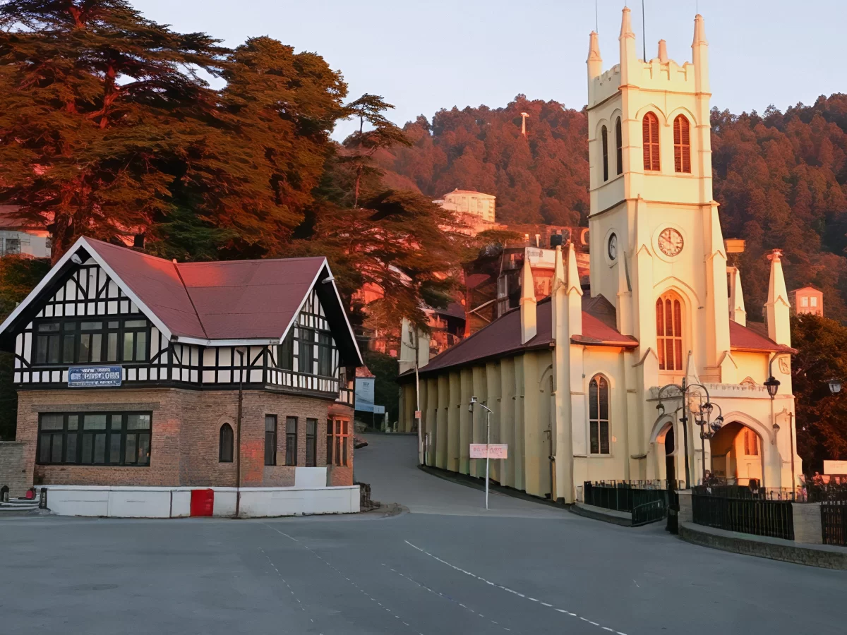 Christ Church The Ridge Shimla during golden hour autumn sunset, featuring yellow Gothic tower clock timbered half-timbered house deodar trees pine hills road lamps railing, perfect colonial heritage cultural experience Himachal Pradesh hill station tour 