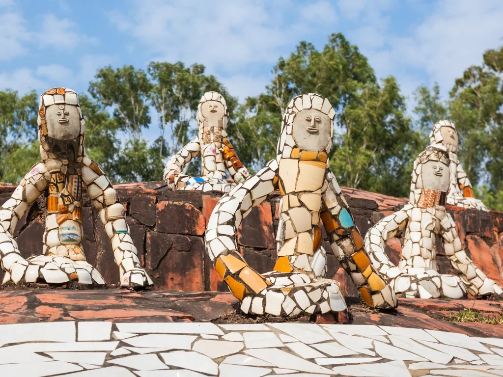 Colorful mosaic sculptures at Rock Garden Chandigarh during sunny day, featuring human figures, trees, rocky base, perfect cultural Himachal Pradesh tour package.