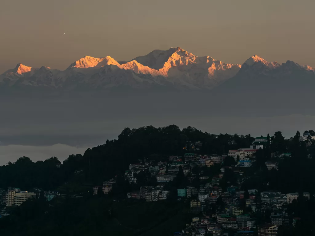 Kanchenjunga view from Tiger Hill in Darjeeling at sunrise, featuring snow peaks glowing above hillside town, perfect Sikkim tour package