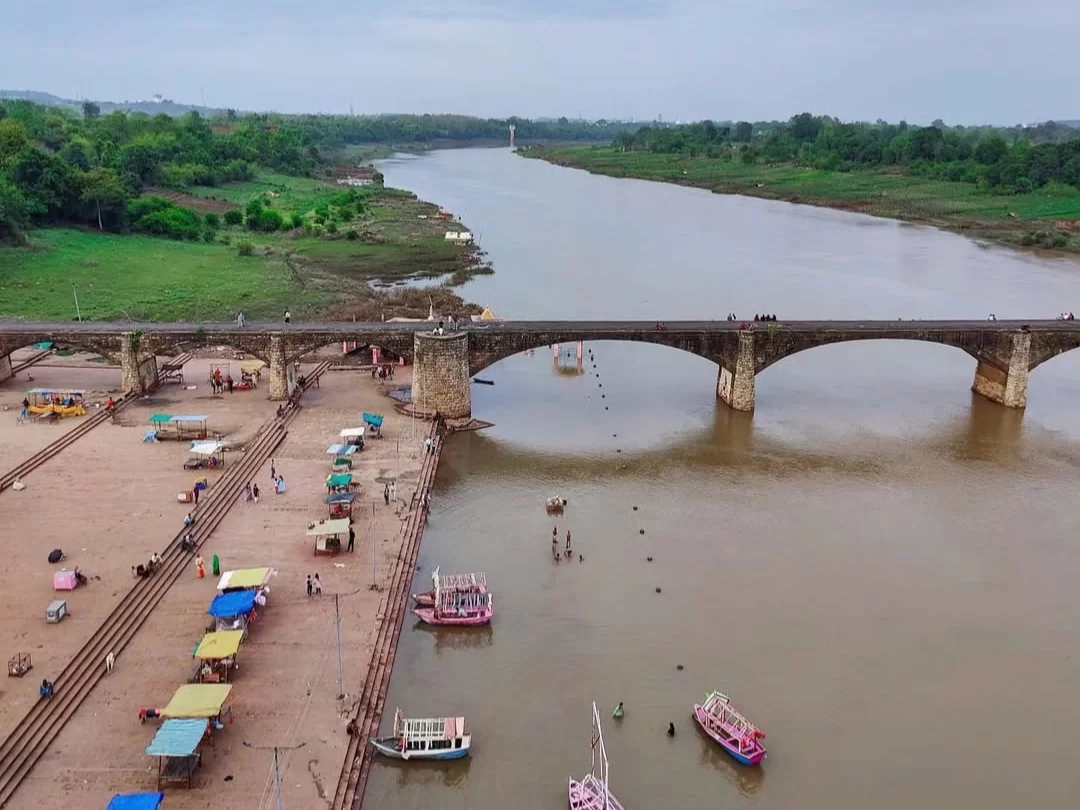 Tilwara Ghat in Jabalpur with stone bridge over the Narmada River, boats along the riverbank, and steps leading to the water, a riverside attraction included in Madhya Pradesh tour packages
