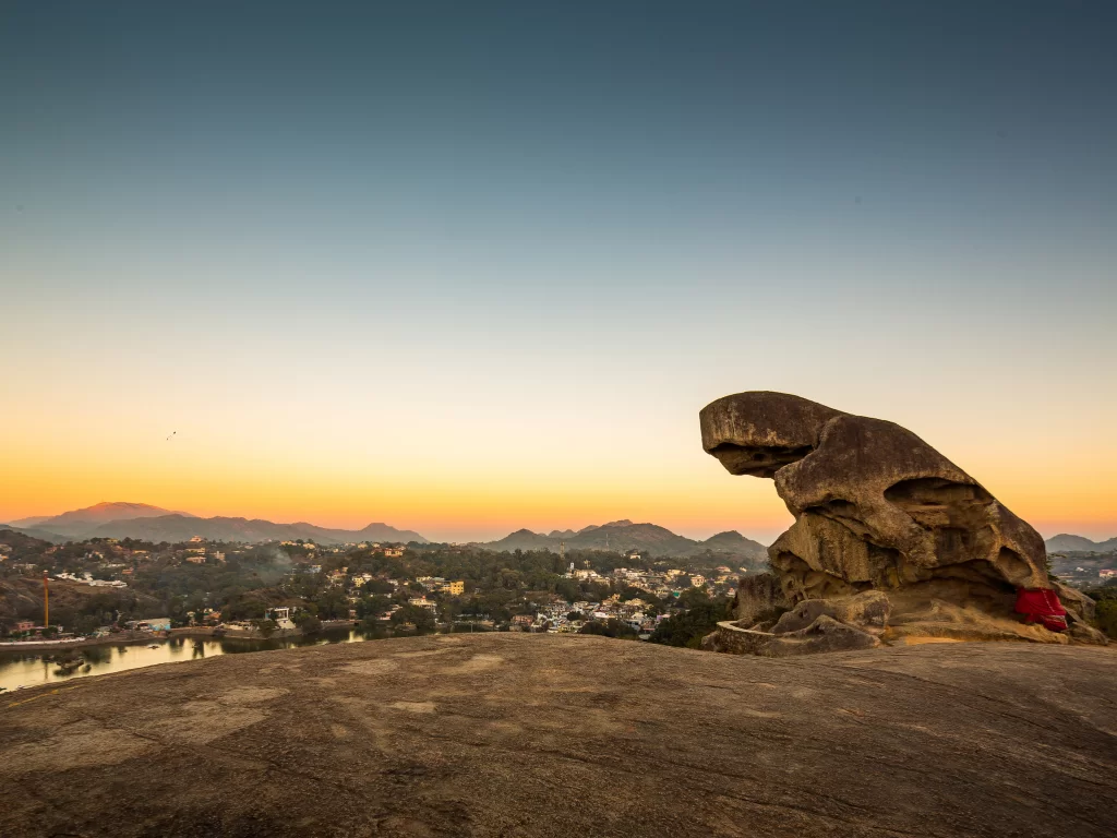 Toad Rock Sunset Point Mount Abu twilight silhouette, featuring toad-shaped boulder overlooking twilight-hued town Nakki Lake distant hills orange sky, perfect Rajasthan tour packages. ​ ​