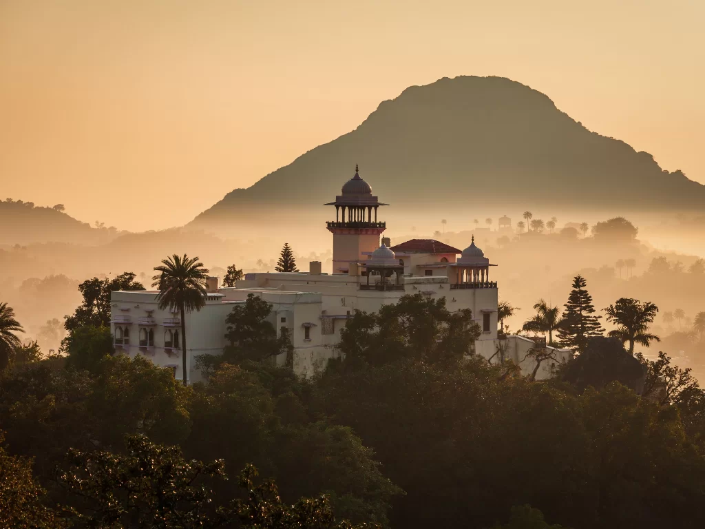 Dilwara Temples Mount Abu sunset silhouette, featuring white marble domes minarets palm trees silhouetted against Achalgarh hill golden mist, perfect Rajasthan heritage tour packages.