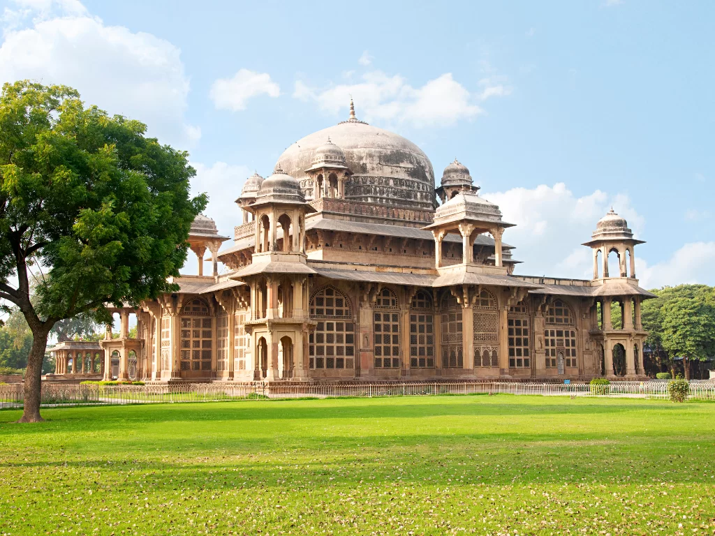 Tomb of Muhammad Ghaus Gwalior during clear afternoon, featuring large central dome with chhatris on square pavilion amid green lawns and trees, perfect heritage experience in Madhya Pradesh tour package.