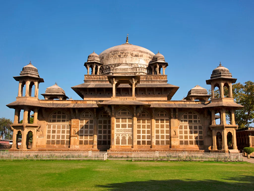 Tomb of Muhammad Ghaus Gwalior during clear afternoon, featuring sandstone Mughal dome with chhatris, lattice jaali screens, and arched verandahs amid manicured lawns, perfect heritage experience in Madhya Pradesh tour package.