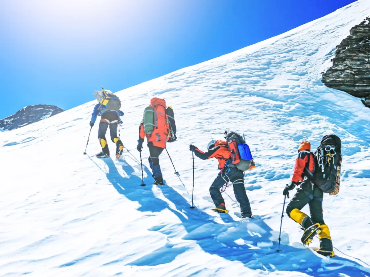 Triund Dharamshala winter trekking group, featuring mountaineers colorful gear trekking poles ascending snowy slopes bright sun blue skies, perfect Himachal Pradesh tour packages.