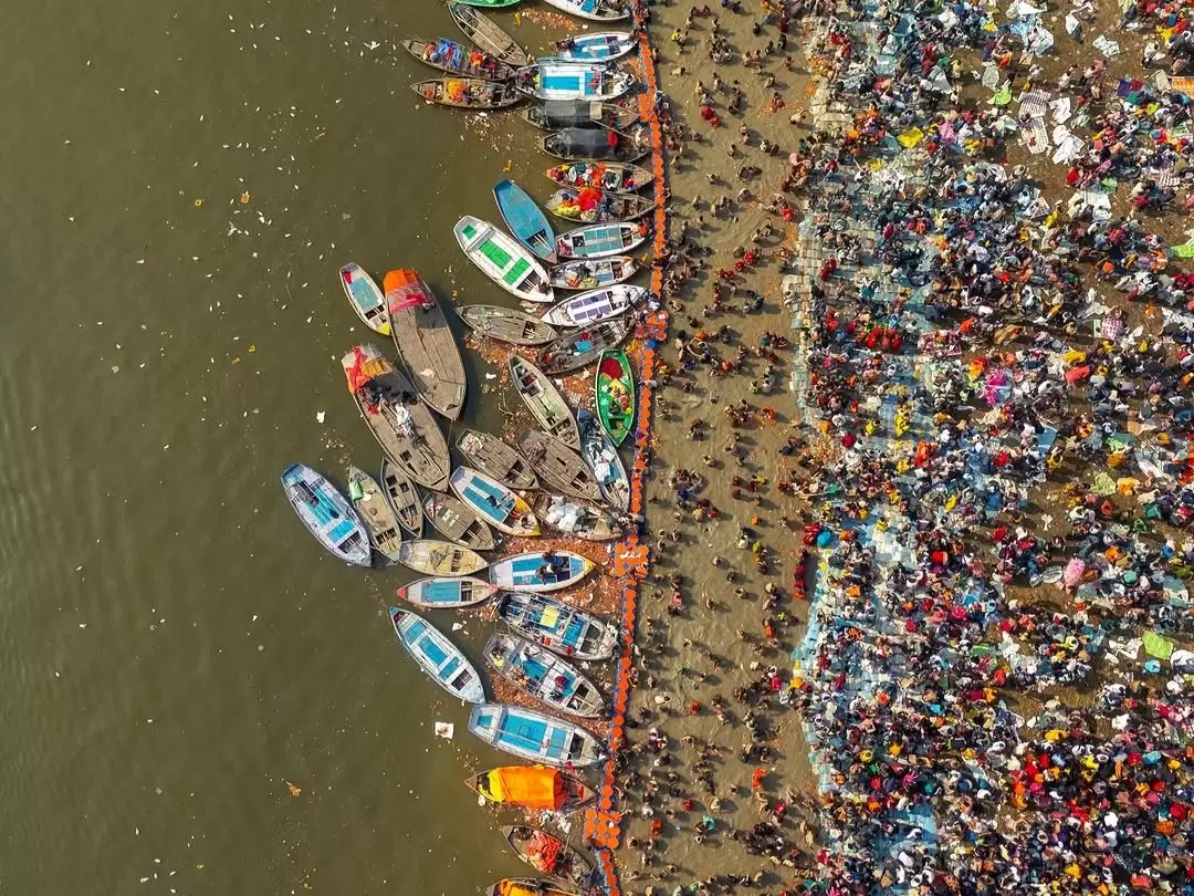 Triveni Sangam aerial Kumbh, colorful boats docked sandy shore pilgrim crowd river, perfect Uttar Pradesh tour package.