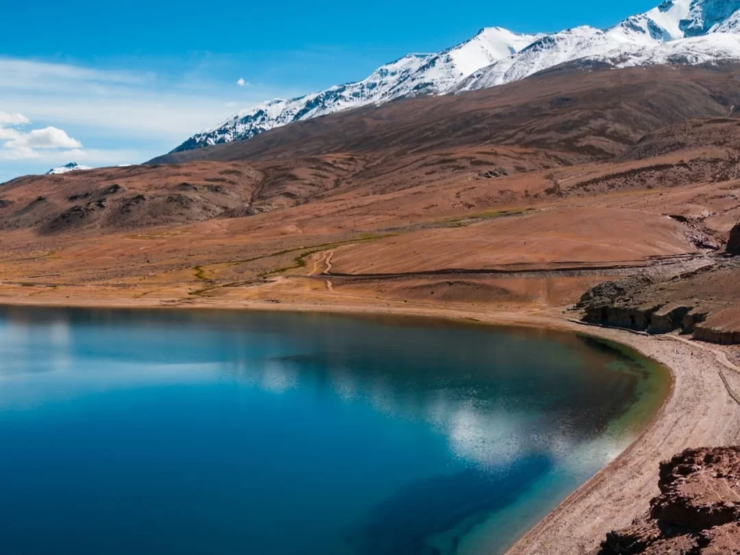 Shoreline of Tso Moriri Lake in Ladakh during clear skies, featuring snow peaks, turquoise waters and barren brown hills, perfect adventure experience with Ladakh tour package. 