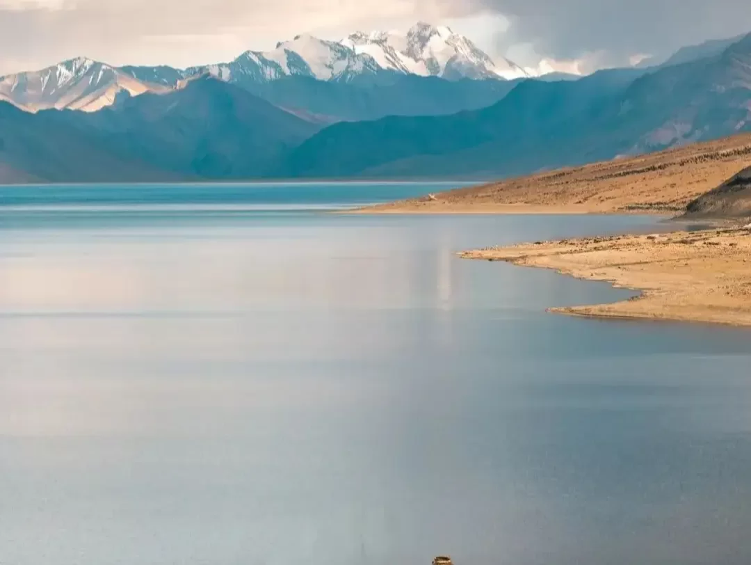 Tso Moriri Lake in Ladakh during cloudy skies, featuring snow-capped peaks reflections in turquoise waters and sandy shores, perfect adventure experience with Ladakh tour package. 