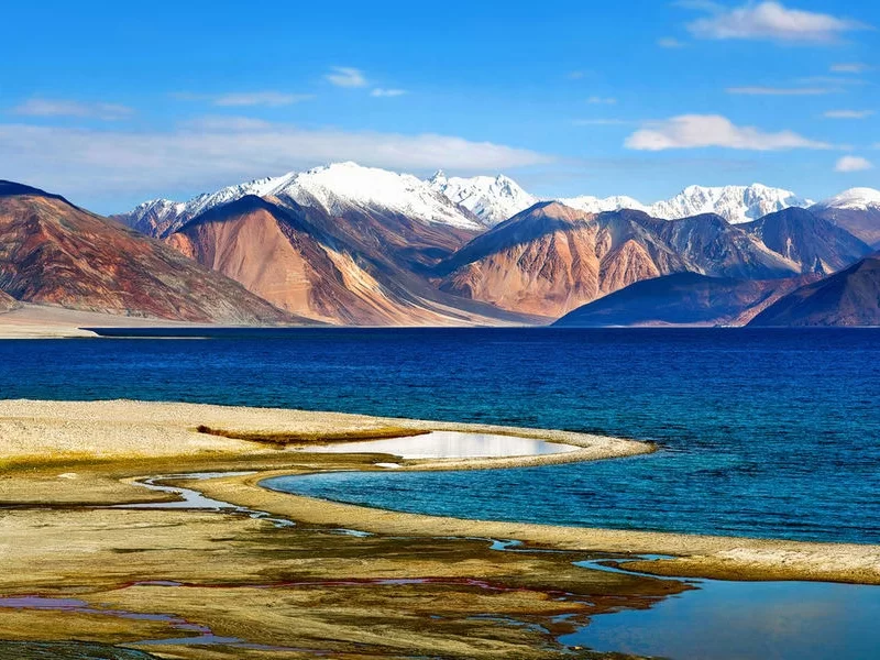 Tso Moriri Lake in Ladakh during clear skies, featuring snow-capped Zanskar mountains, turquoise waters and sandy spits, perfect serene adventure with Ladakh tour package. 
