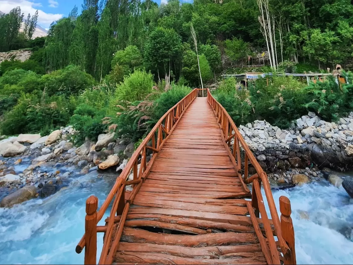 Scenic wooden suspension bridge over turquoise river in lush green forested valley of Turtuk village Nubra Ladakh, surrounded by rocky boulders and mountains, perfect adventurous nature trek with Ladakh tour package.