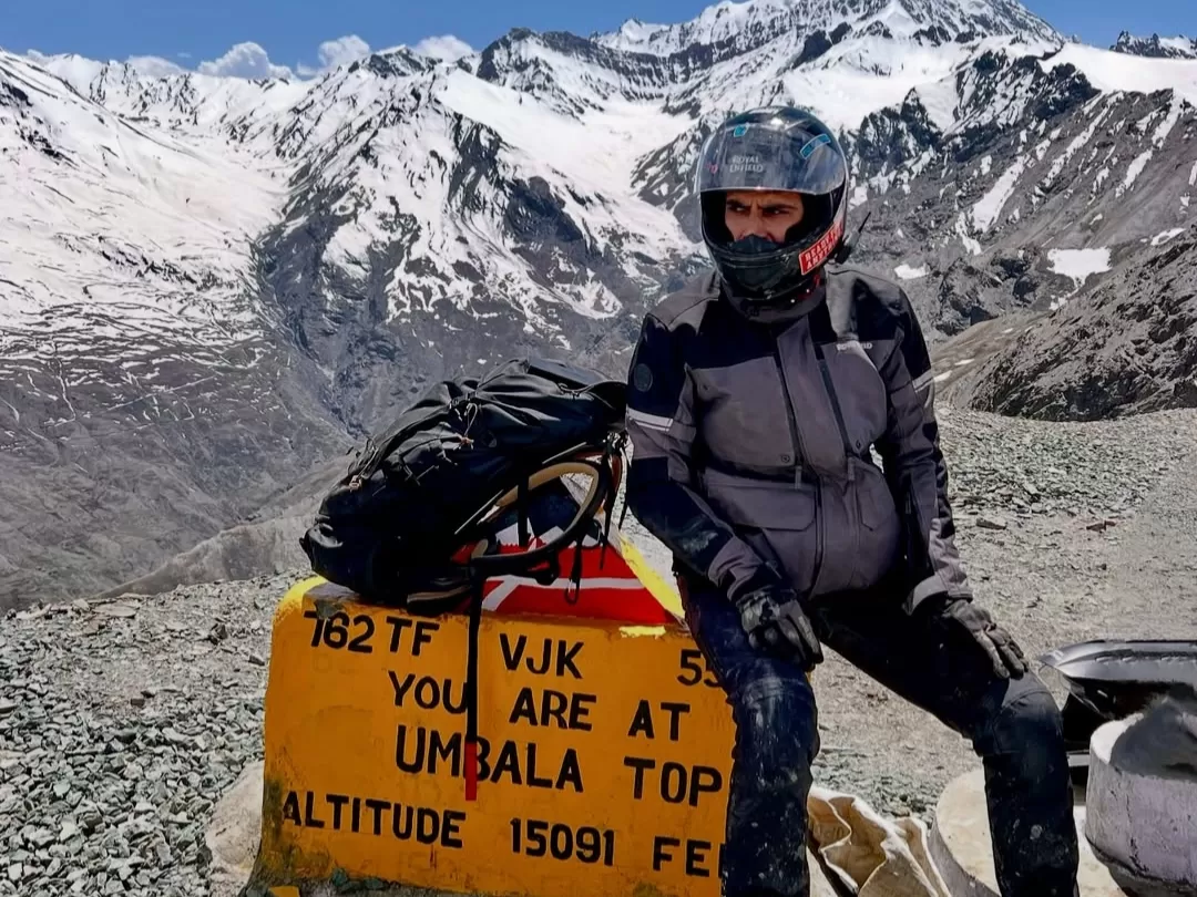 Umba La Top altitude 15091 ft biker helmet backpack posing yellow signboard 162 TF VJK snowy Himalayan peaks blue sky gravel foreground; motorbike adventure Kargil Ladakh photography package.