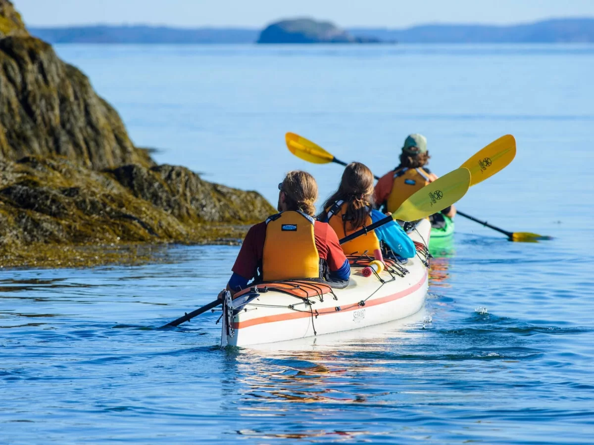 Kayaking adventure at Umkhali Water Park Mawlynnong Meghalaya during sunny day, featuring blue lake rocky shores yellow paddles islands, perfect water adventure Meghalaya tour package.
