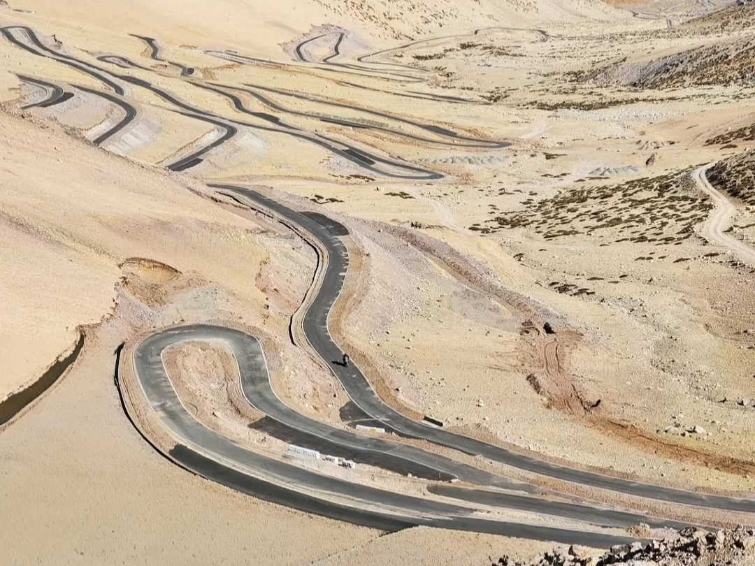 Winding roads at Umling La Pass Ladakh in clear weather, featuring serpentine blacktop paths and barren hills, perfect adventure Ladakh tour package.