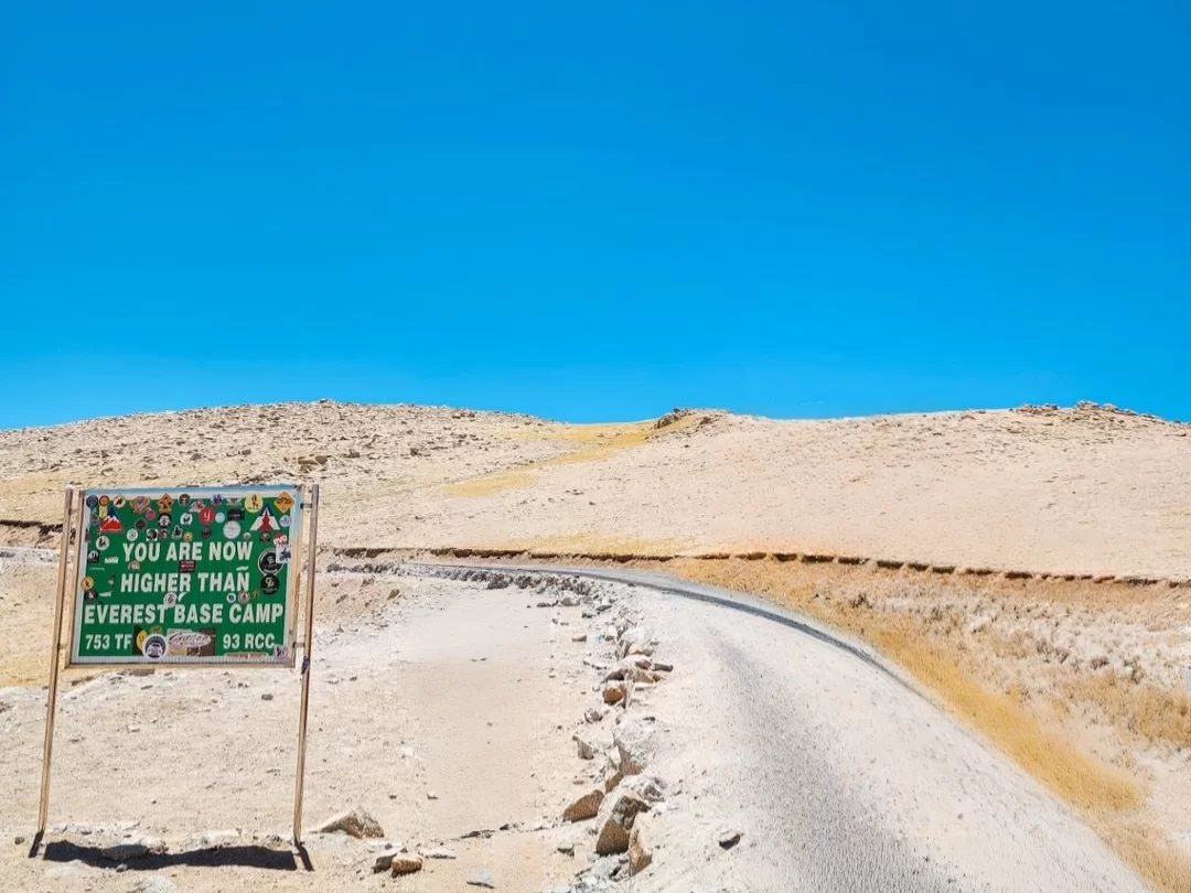 than Everest Base Camp sign at Umling La Pass Ladakh in sunny skies, featuring green board and dirt road hills, perfect adventure Ladakh tour package
