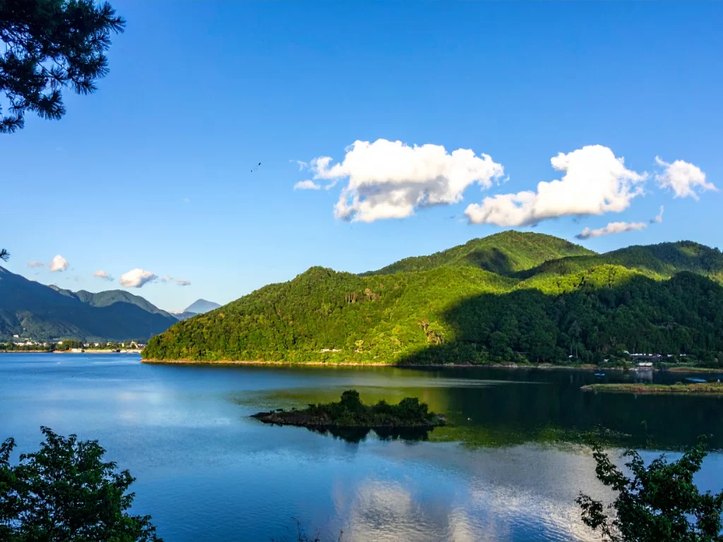 Valvan Lake View Point scenic foreground trees framing turquoise lake lush green forested hills mountains under partly cloudy blue skies, perfect Lonavala Maharashtra nature tour packages.