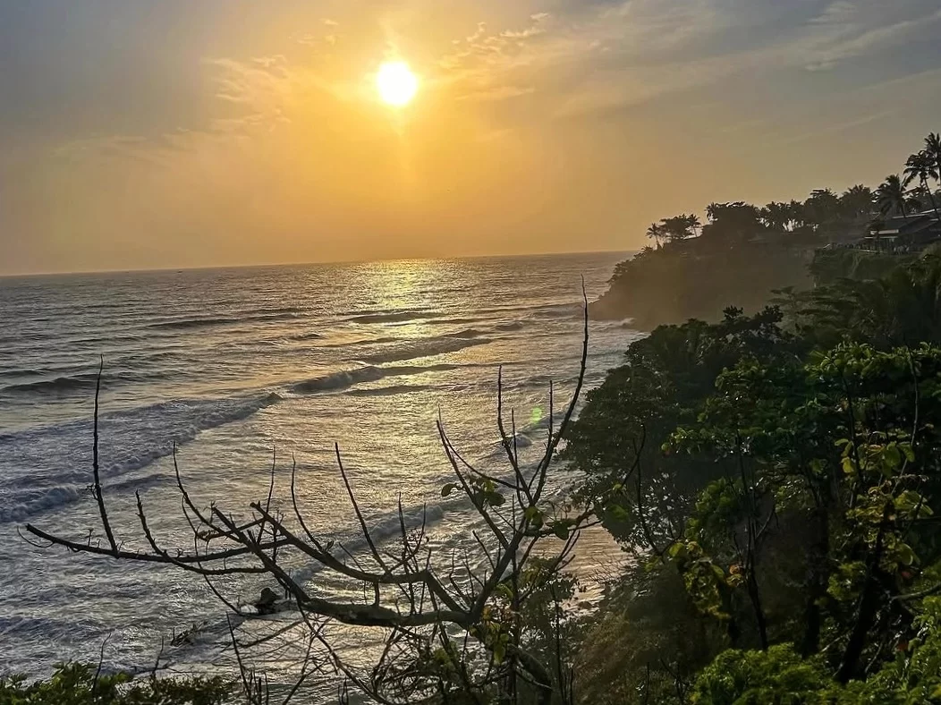 Varkala Cliff in Kerala, scenic sunset view over Arabian Sea with palm trees and waves below.