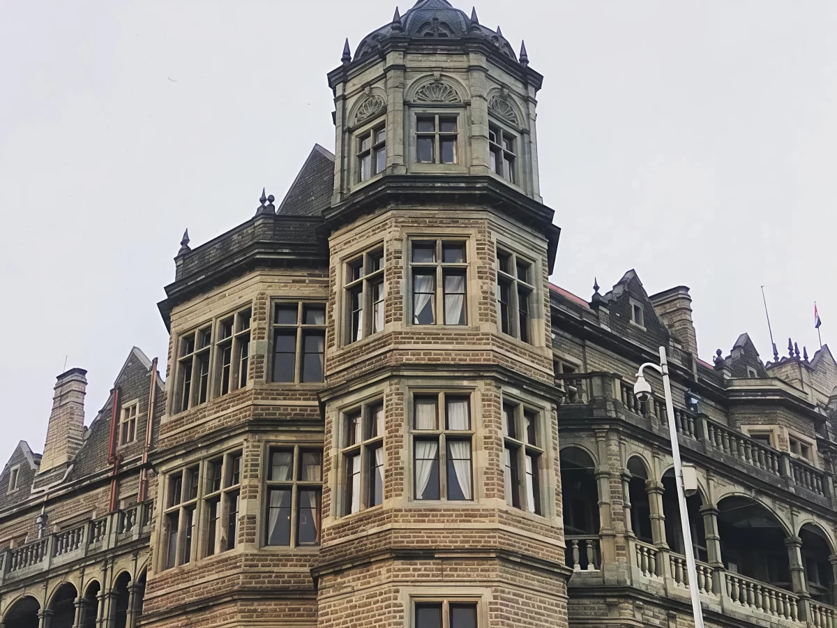Viceregal Lodge Shimla detailed turreted corner during misty day, featuring arched windows red roof ornate stonework lamp post, perfect heritage romantic experience Himachal tour packages.