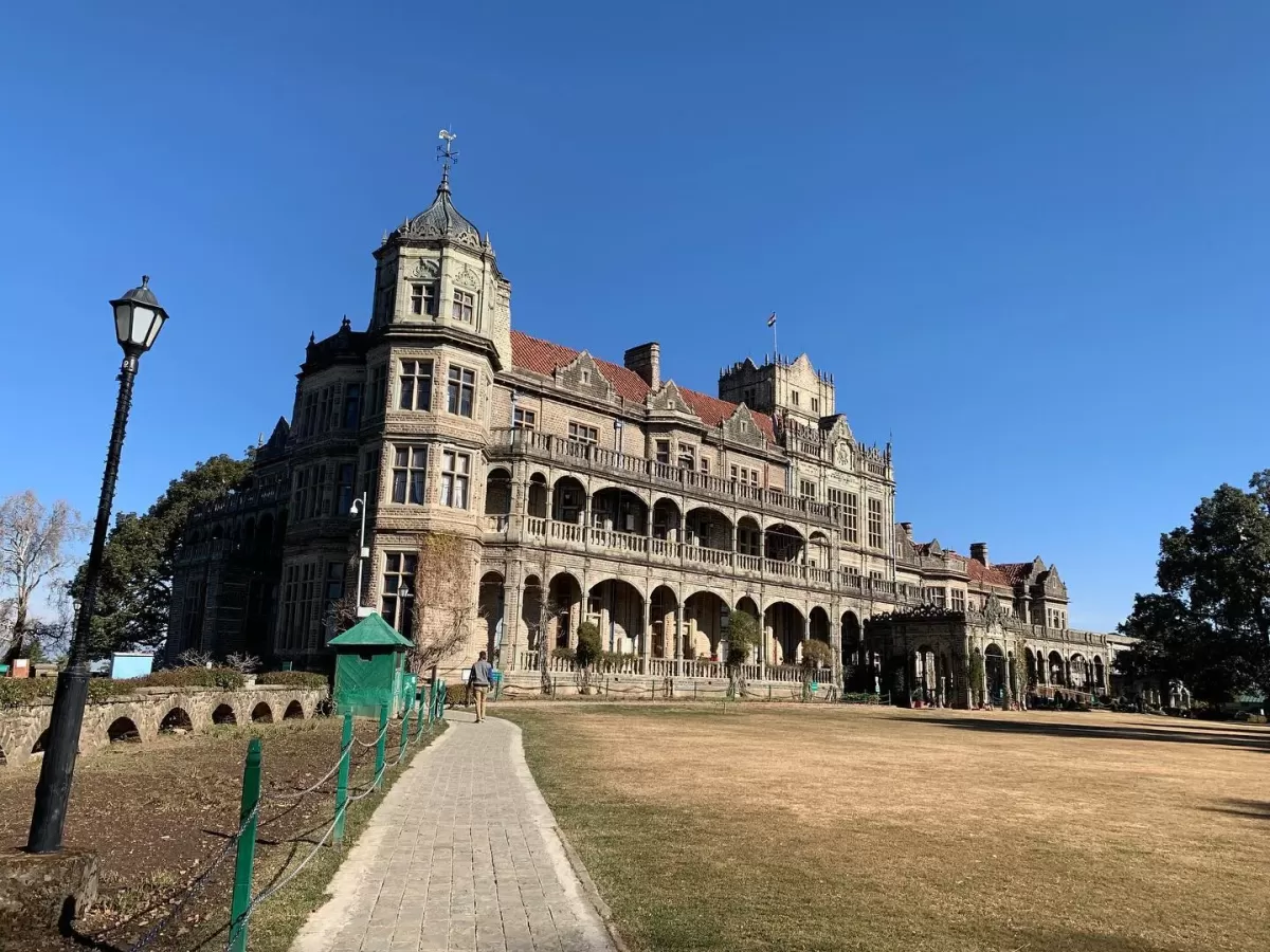 Viceregal Lodge Shimla stunning colonial building during clear blue sky day, featuring turret red roofs arched verandas dry grass path tourists, perfect heritage romantic experience Himachal tour packages.