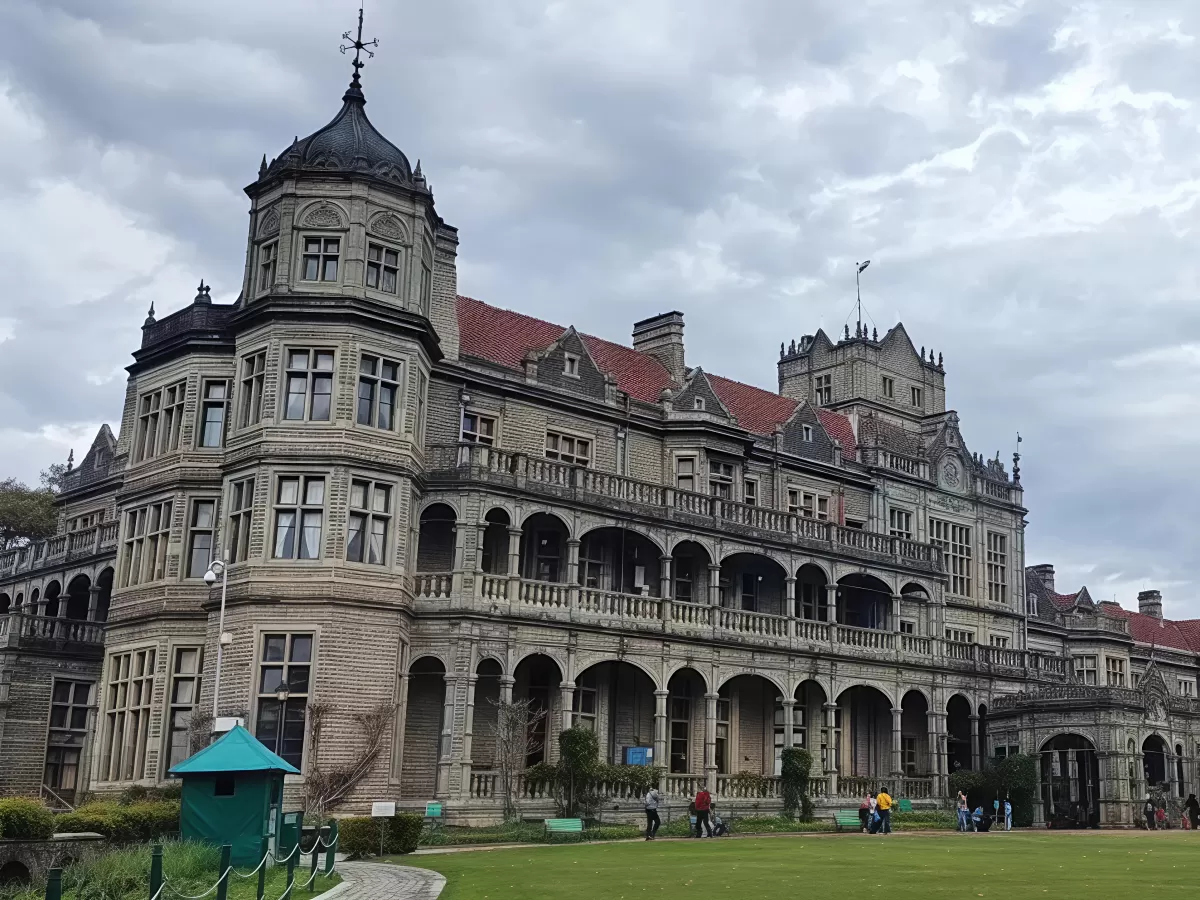 Viceregal Lodge Shimla majestic colonial facade during cloudy day, featuring turret red roofs arched balconies green lawns tourists walking, perfect heritage romantic experience Himachal tour packages.