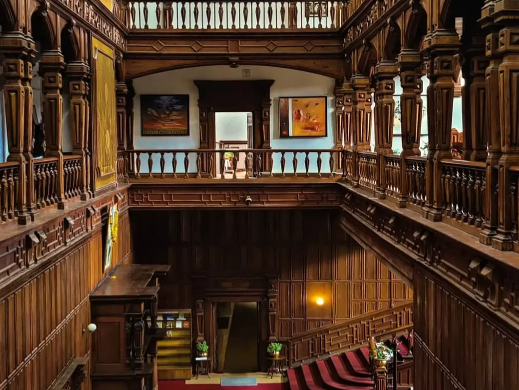 Viceregal Lodge Shimla opulent wooden interior atrium during day, featuring carved pillars paintings red carpet balcony railing, perfect heritage romantic experience Himachal tour packages.