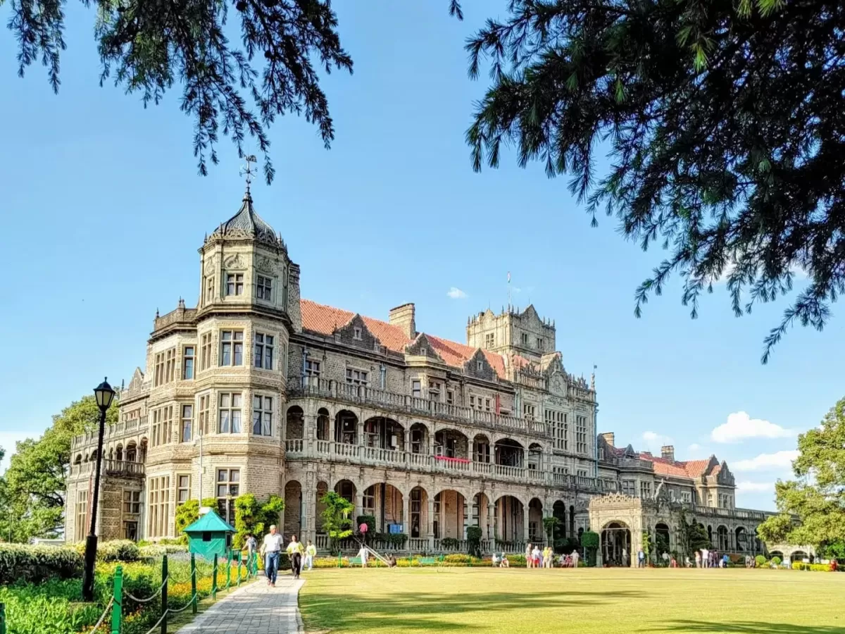 Viceregal Lodge Shimla grand colonial mansion sunny day with tourists, featuring red roofs arched balconies manicured lawns pine trees, perfect heritage romantic experience Himachal tour packages.