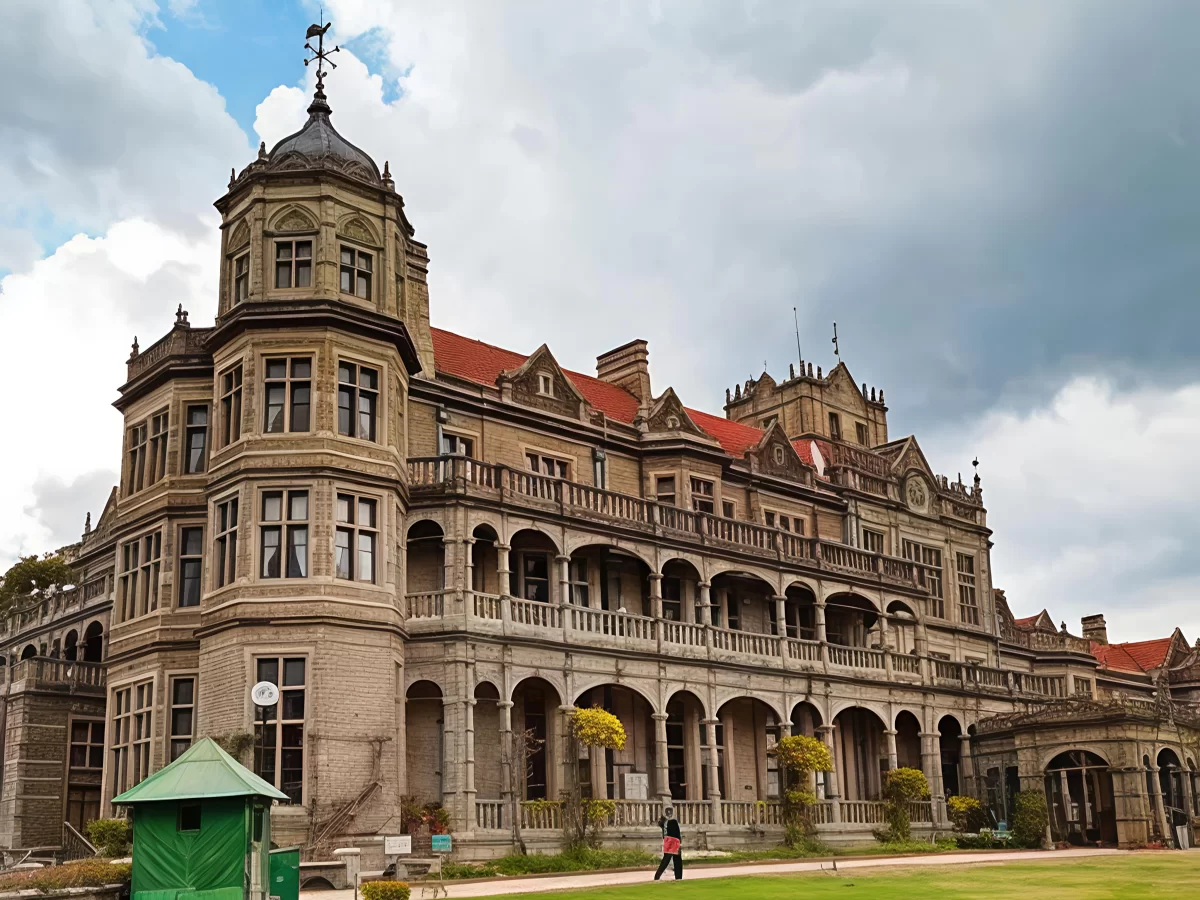Viceregal Lodge Shimla grand colonial architecture during partly cloudy day, featuring red roofs arched verandas manicured lawns person walking, perfect heritage romantic experience Shimla tour packages.