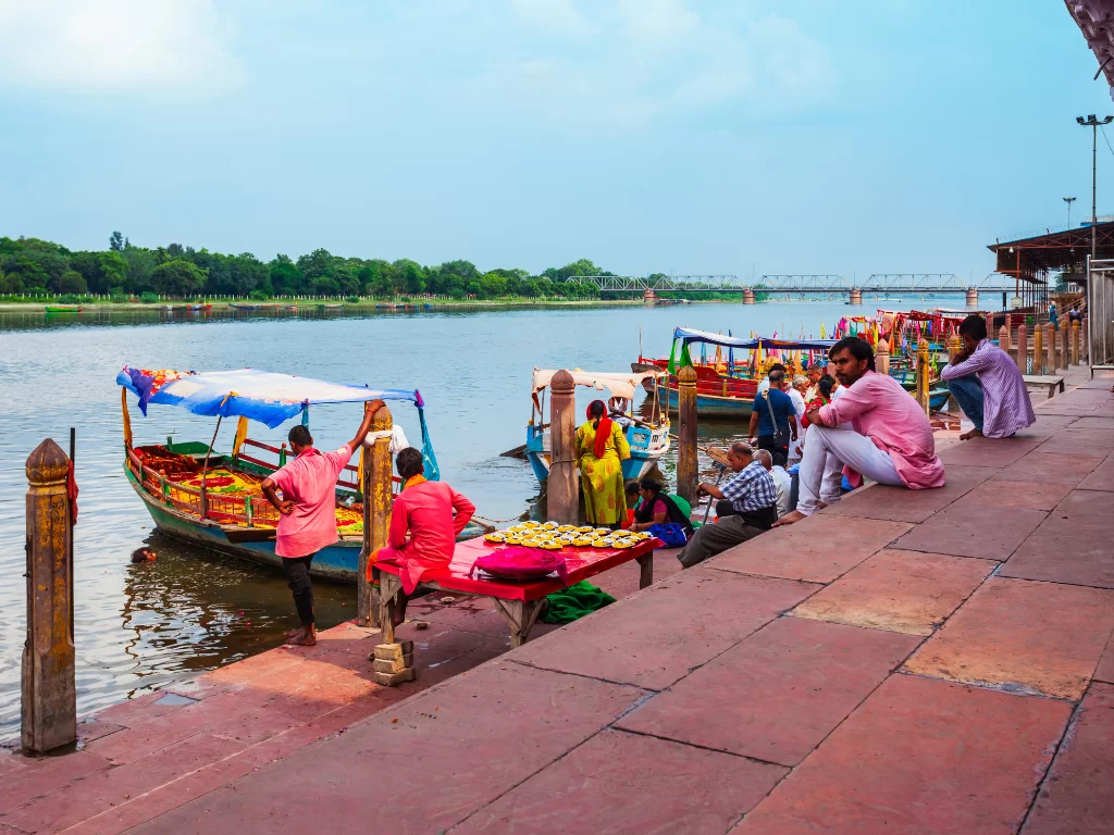 Boats and vendors at Vishram Ghat Mathura on Yamuna River in clear skies, featuring colorful flower boats and ghats, perfect cultural Mathura Vrindavan tour package.