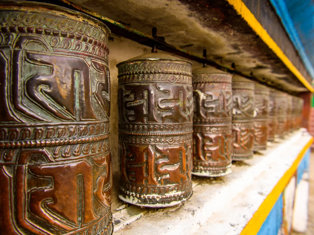 Prayer wheels at Yiga Choeling Monastery in Darjeeling during daytime, featuring rustic metal carvings and vibrant colors, perfect spiritual Darjeeling tour package