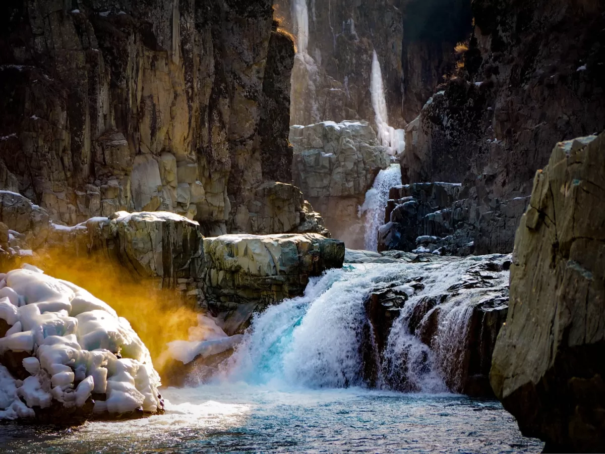 Aharbal Waterfall, known as Kashmir's Niagara, features multi-tiered icy cascades in dramatic winter gorge golden sunlight rocky cliffs. 
