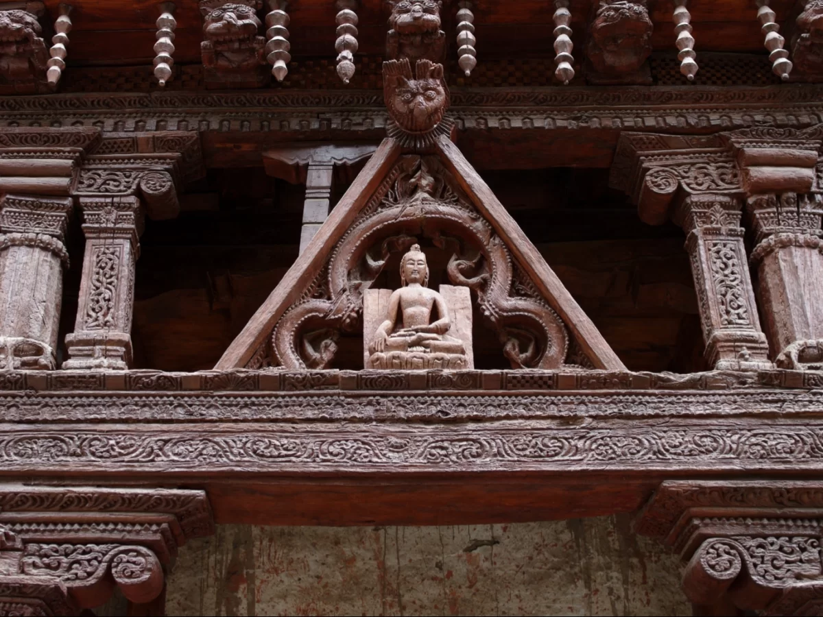 Buddha statue at Alchi Gompa during daylight, featuring intricate wooden carvings, triangular arch, and ornate temple brackets, perfect spiritual experience for Ladakh tour package. 