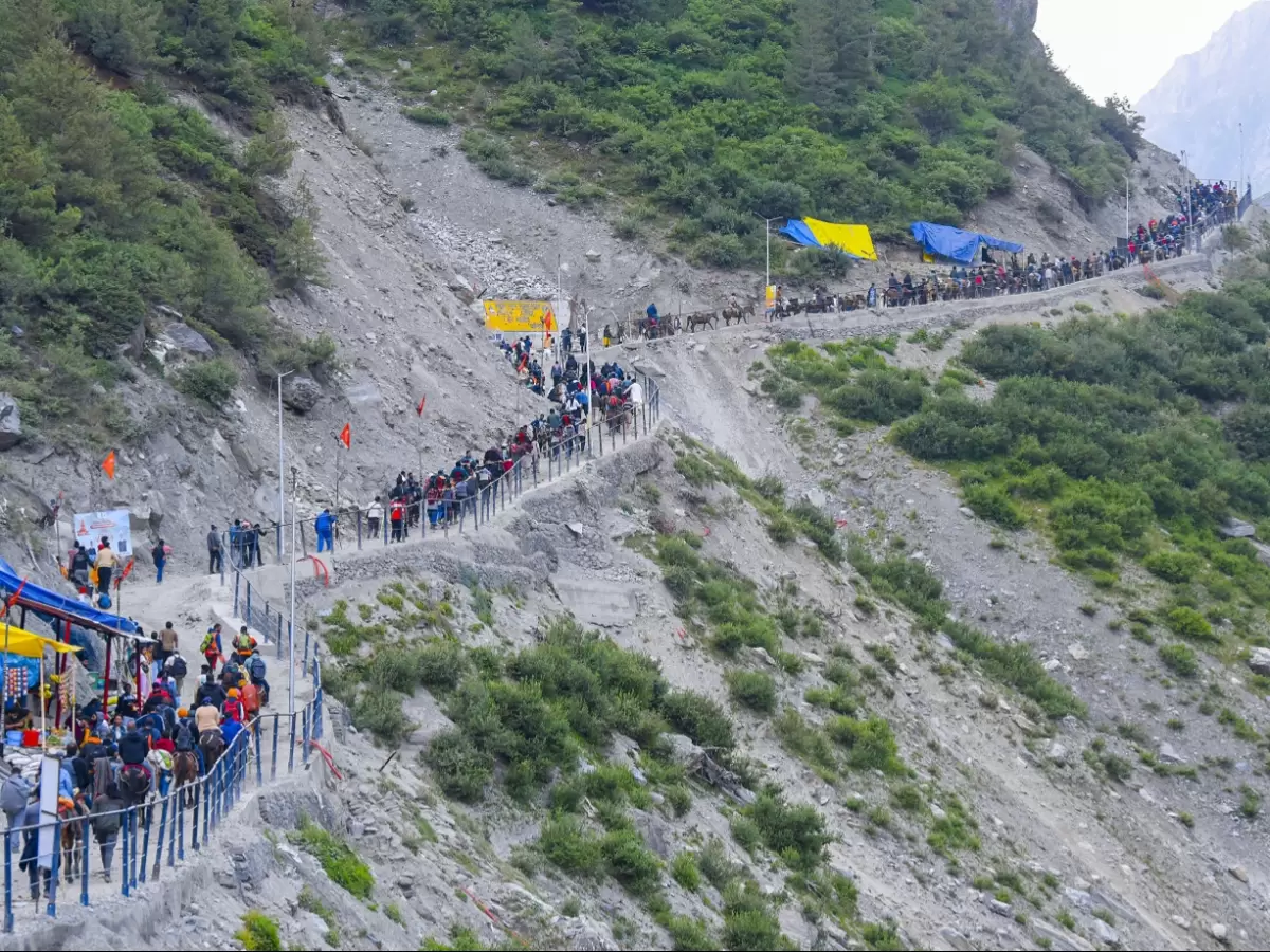 Amarnath Yatra pilgrims winding steep mountain trail blue yellow tents, railings rocky slopes green bushes clouds, perfect Jammu Kashmir high altitude spiritual trek package.