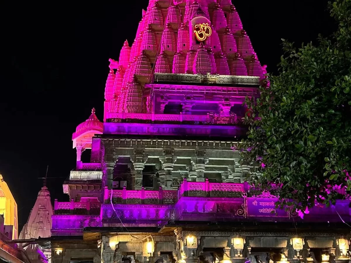 Shree Mahakaleshwar Temple at Ujjain during night illumination, featuring pink glowing shikhar golden Om symbol, perfect spiritual Madhya Pradesh tour package.