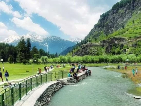 Tourists along Lidder River at Betaab Valley Pahalgam during sunny day, featuring green meadows mountains and turquoise waters, perfect adventure experience Kashmir tour packages.