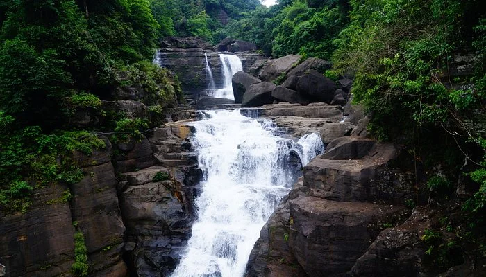 Borhill Falls near Dawki featuring multi-tiered cascading waterfall, dramatic rock formations, and lush green forest canopy, perfect nature experience with Meghalaya tour package.