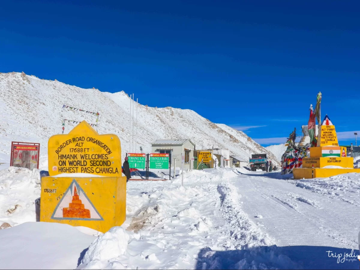 BRO sign World’s Second Highest Motorable Pass Changla at 17688 ft during sunny skies, featuring snow-covered road, stupas, perfect adventure Ladakh tour pack