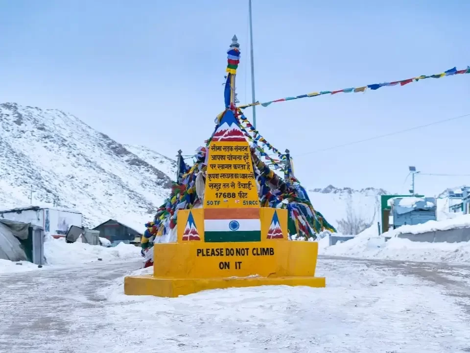 Memorial at Changla Pass 17688 ft during overcast skies, featuring prayer flags, Indian tricolor, snowy mountains, perfect spiritual adventure Ladakh tour pack
