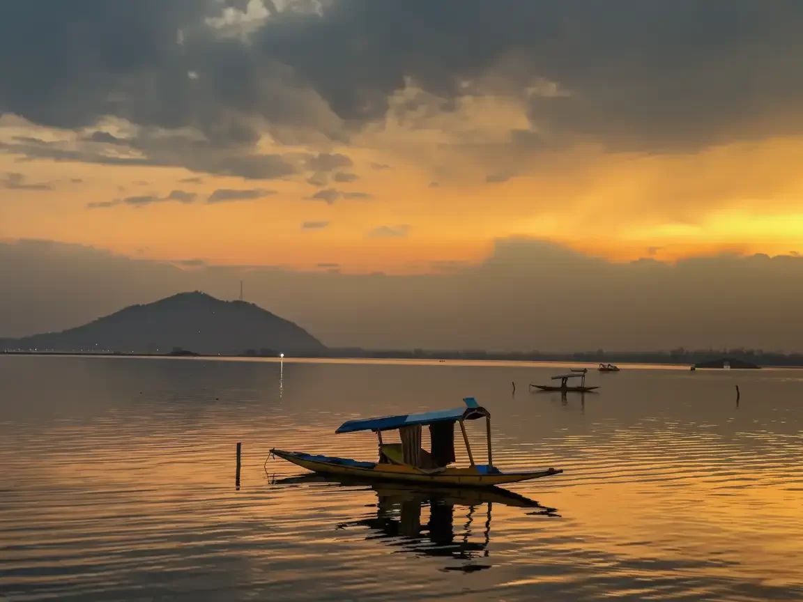 Shikara boat sunset silhouette Dal Lake Srinagar with Zabarwan mountains hazy clouds reflection featured in Kashmir Srinagar tour packages