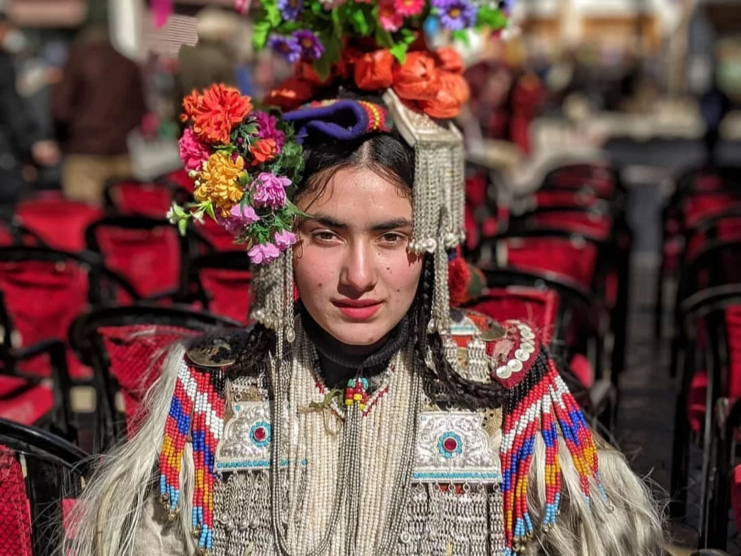 Dha Hanu Brokpa Ladakh woman floral headdress vibrant flowers silver jewelry traditional dress red chairs, perfect Aryan Valley cultural trek heritage photography package. 