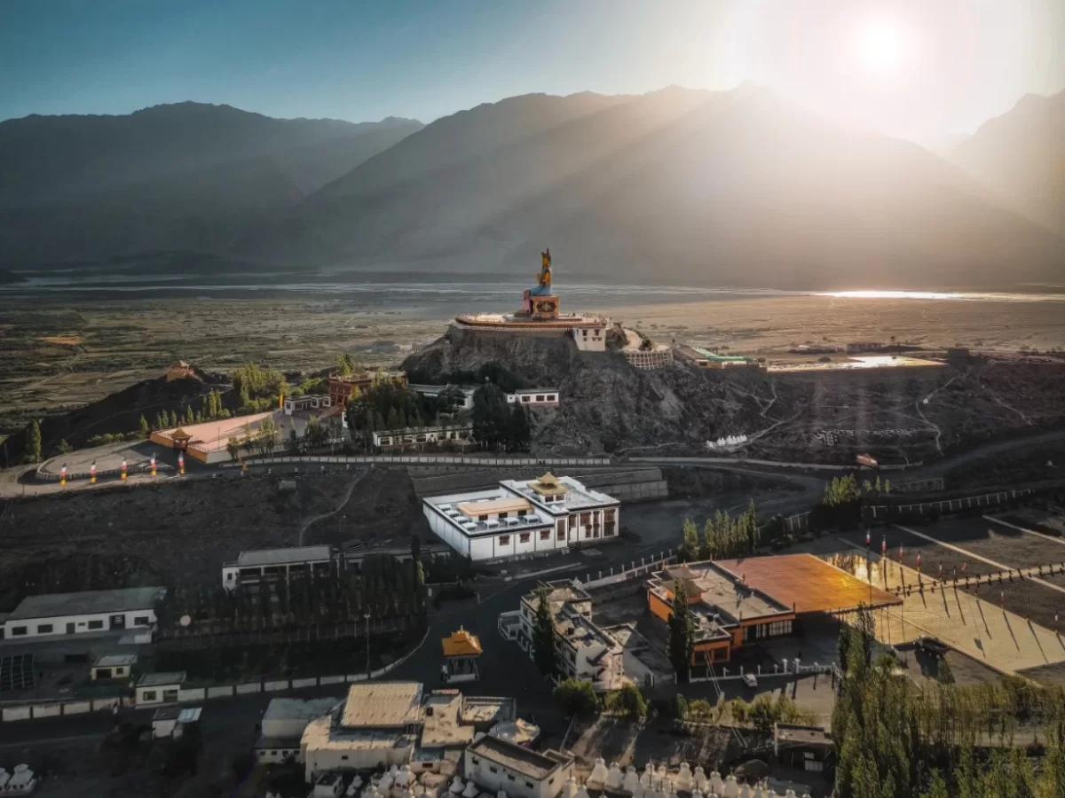 Diskit Gompa Ladakh aerial view golden Maitreya Buddha statue sunset Shyok River valley monasteries rugged mountains Nubra Valley, perfect Leh Ladakh spiritual adventure package.