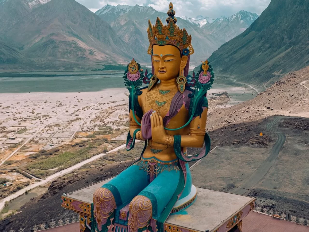 Diskit Gompa Ladakh aerial golden Maitreya Buddha statue prayer pose snowy peaks Shyok River Nubra Valley desert, perfect Leh Ladakh spiritual adventure package.