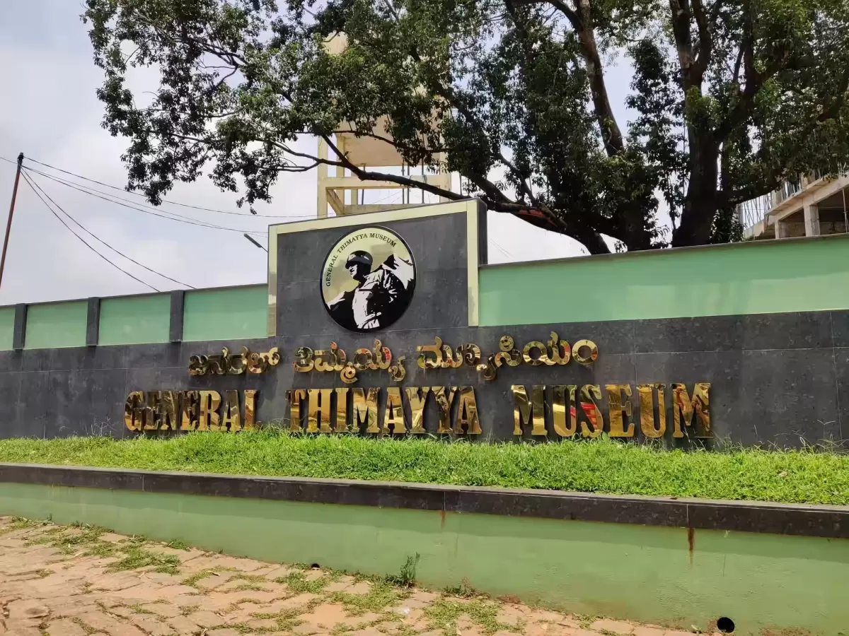 General Thimayya Memorial Museum at Madikeri Coorg during sunny day, featuring entrance sign, portrait, trees, compound wall, perfect cultural experience Karnataka tour packages.